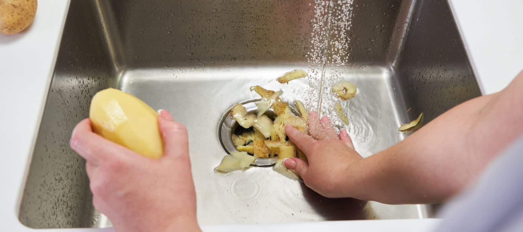 person peeling potatoes over their sink and pushing the skin down the drain