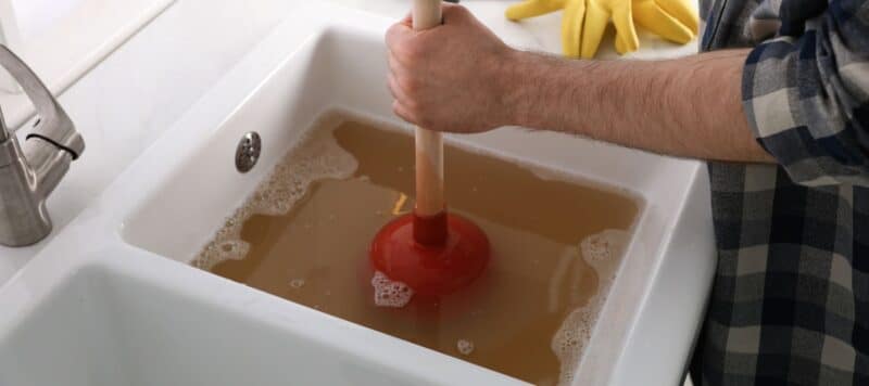 Person using a plunger to clear a clogged sink with standing water