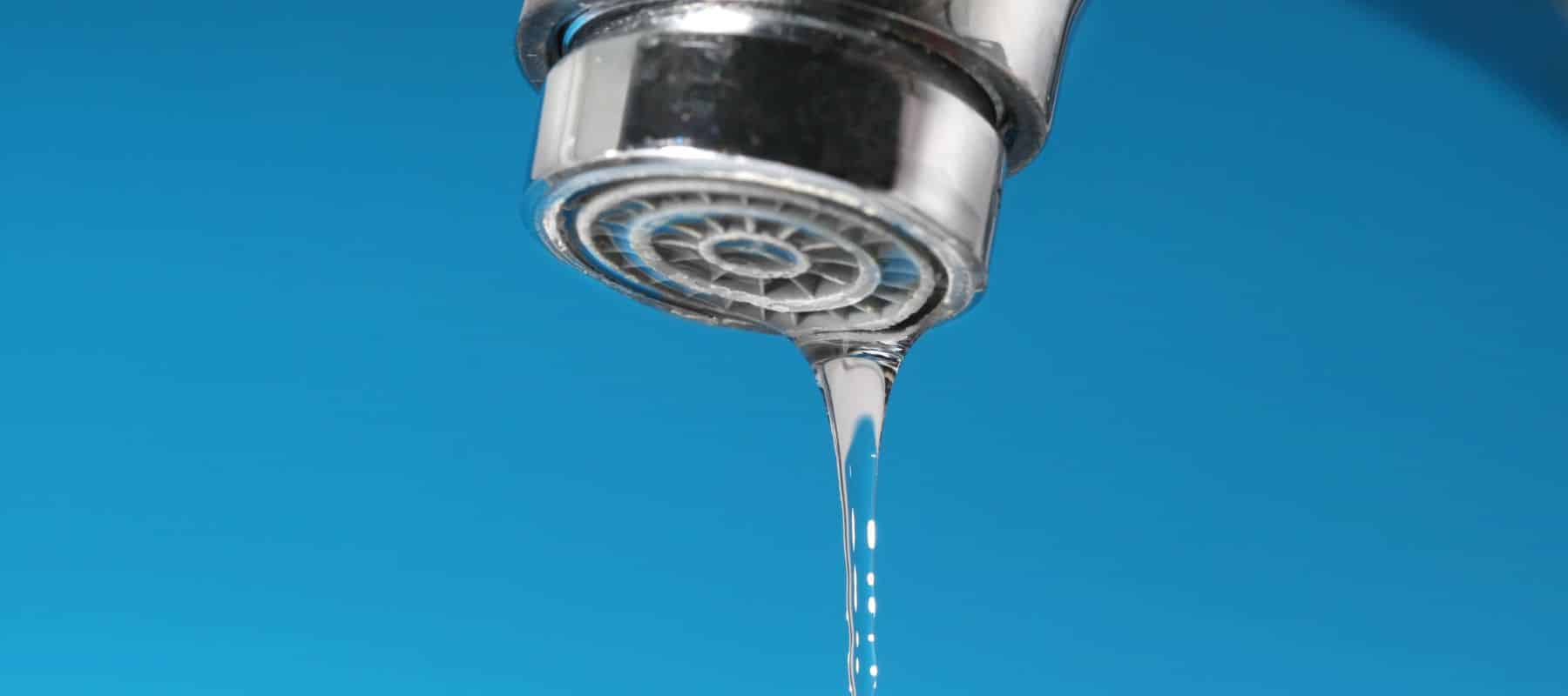 closeup of a water faucet dripping water in front of a blue background