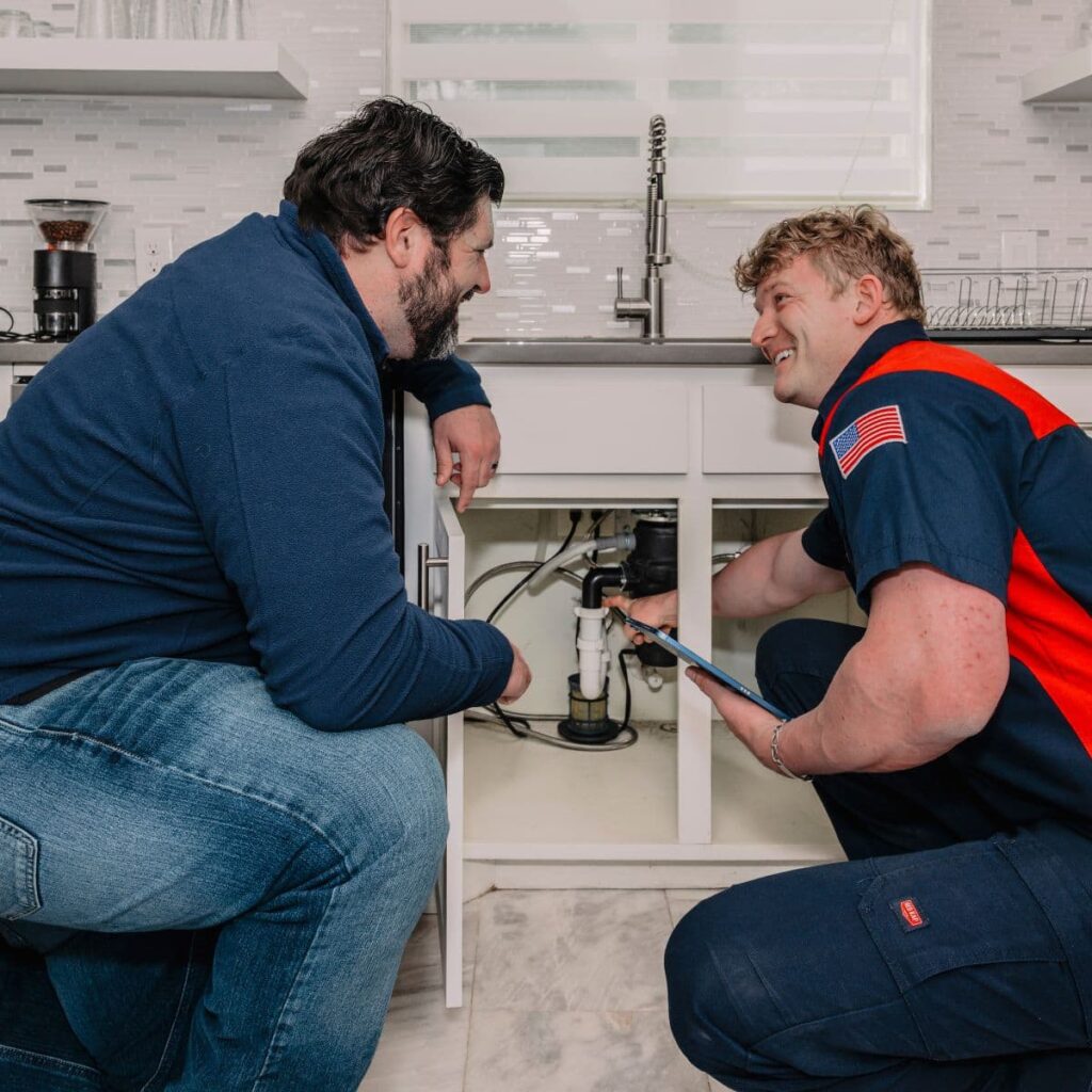 Technician showing disposal system to customer under kitchen sink