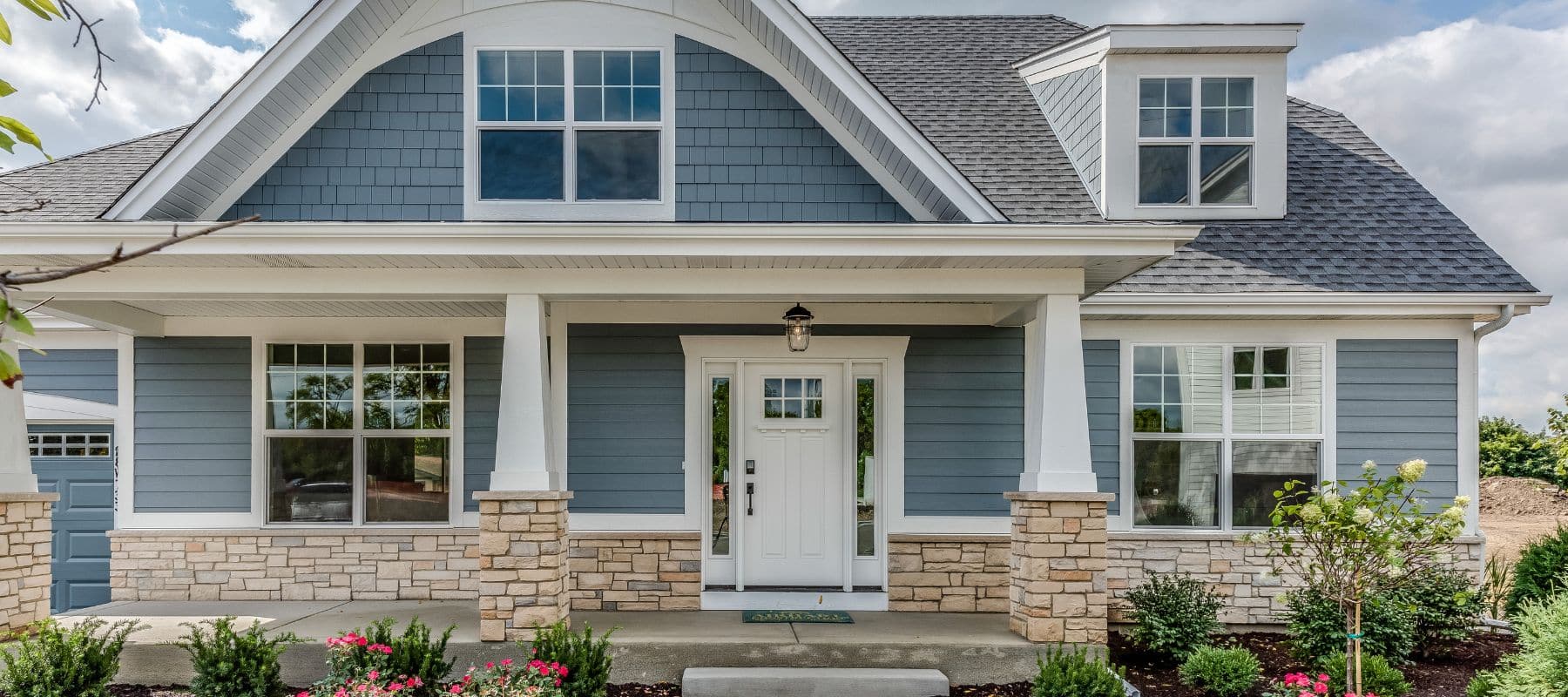 The inviting front facade of a two-story home showcases blue siding, white trim, stone accents, and a prominent white front door with multiple windows