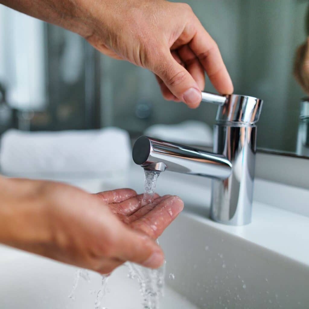 Person washing hands under running bathroom faucet