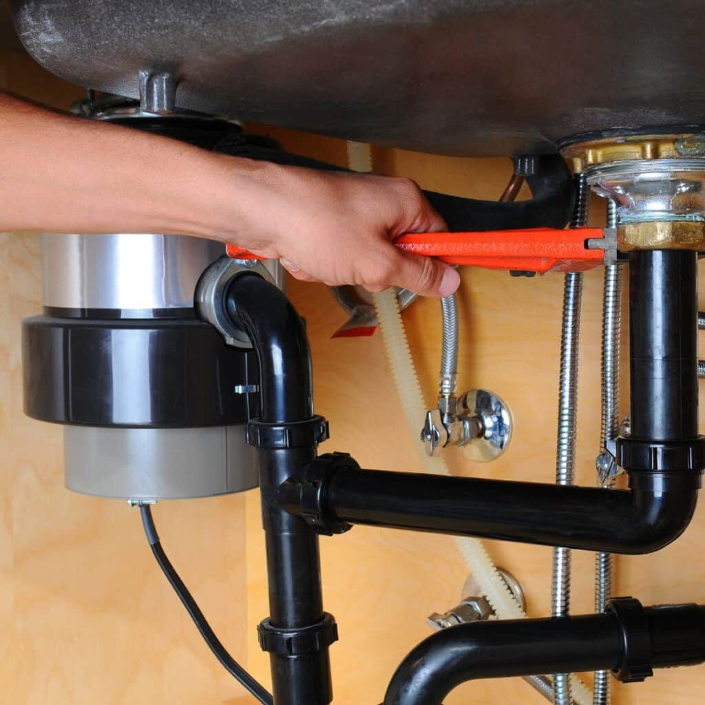 Plumber using a wrench to tighten a garbage disposal connection under the sink