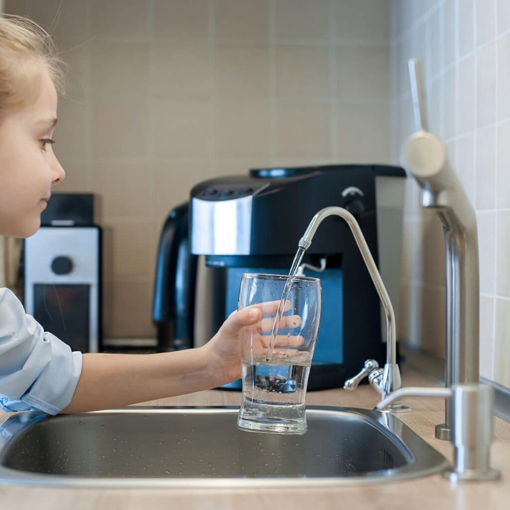 Child filling a glass with filtered water from a reverse osmosis faucet in the kitchen