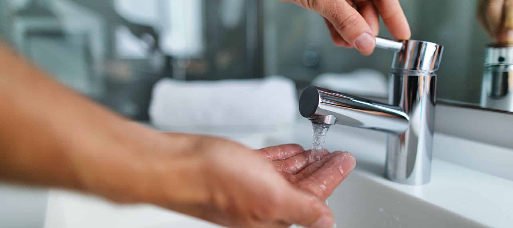 Person washing hands under running bathroom faucet