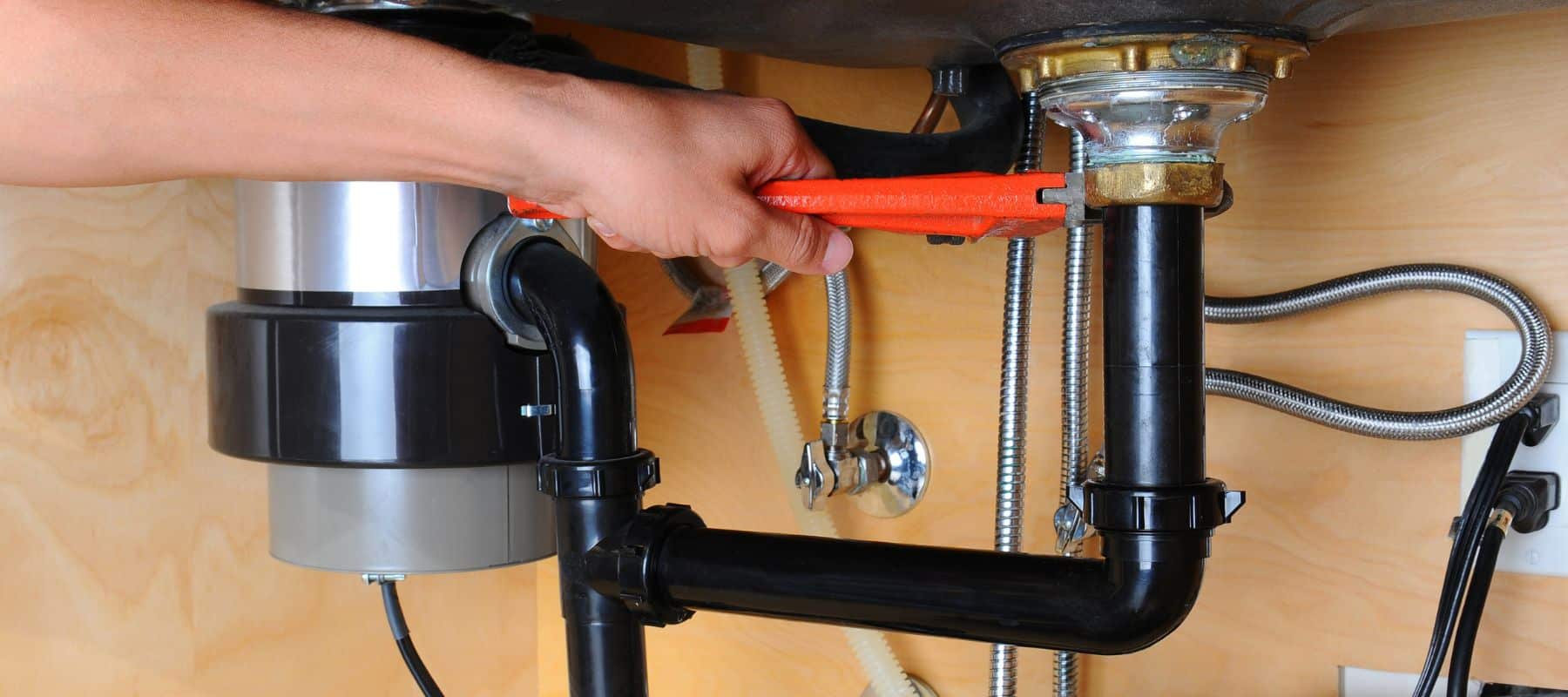 Plumber using a wrench to tighten a garbage disposal connection under the sink