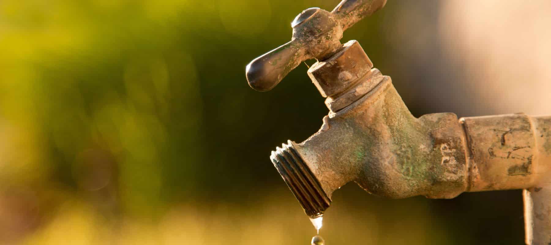 Old outdoor water faucet dripping with a blurred green background