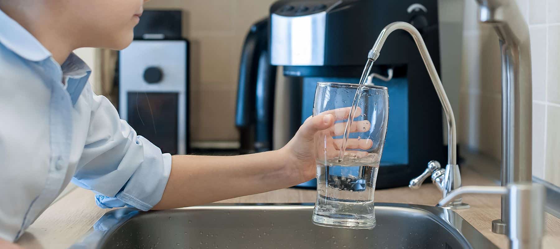 Child filling a glass with filtered water from a reverse osmosis faucet in the kitchen