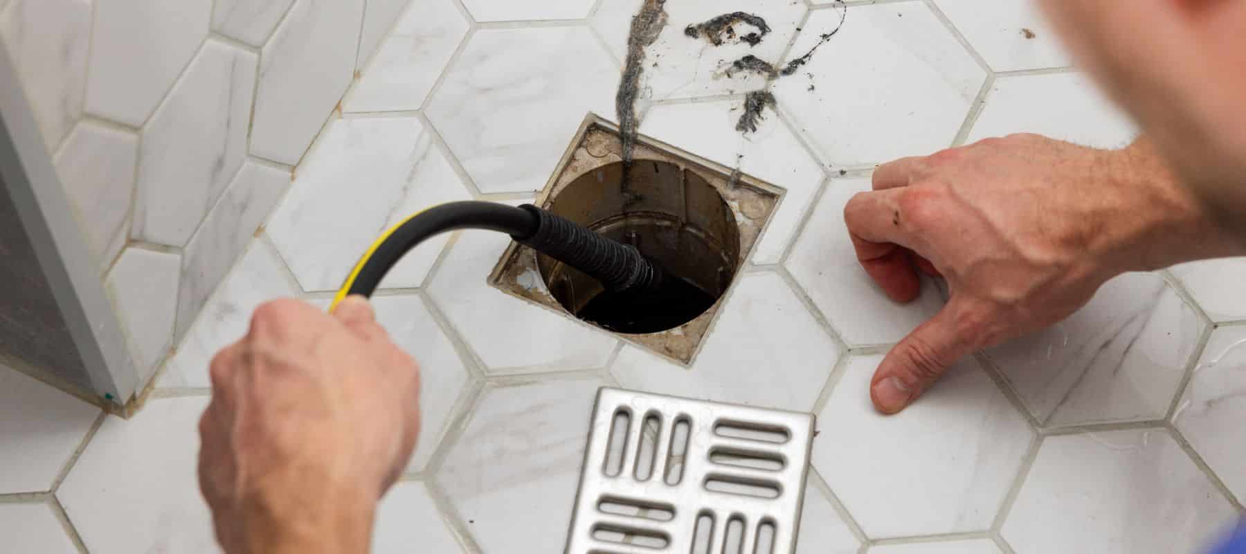 Plumber using a tool to clear a clogged shower drain on tiled floor
