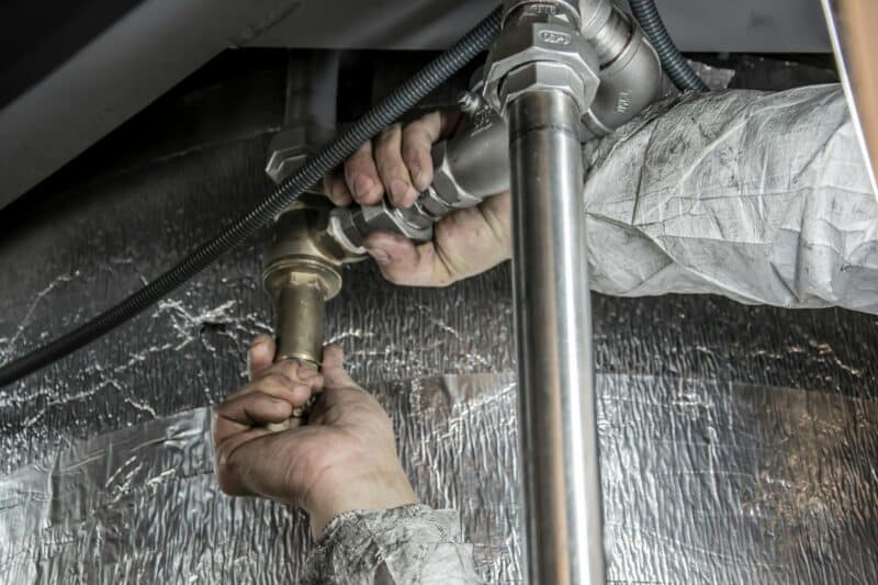 Plumber installing drain pipe fittings under a home