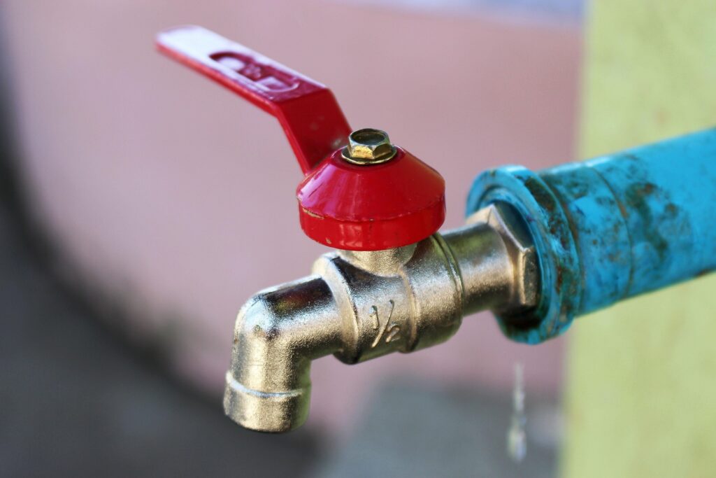 Close-up of a brass outdoor faucet with a water drop visible at the spout - How Much Does a Plumber Cost?