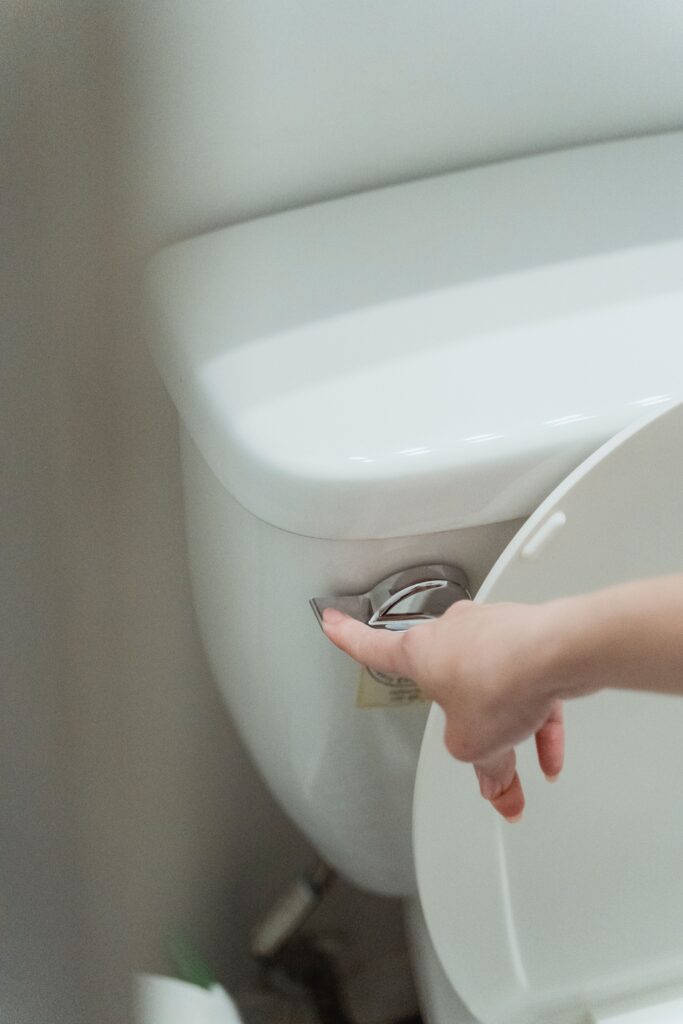 Hand pressing a toilet flush handle while troubleshooting a toilet that keeps running.