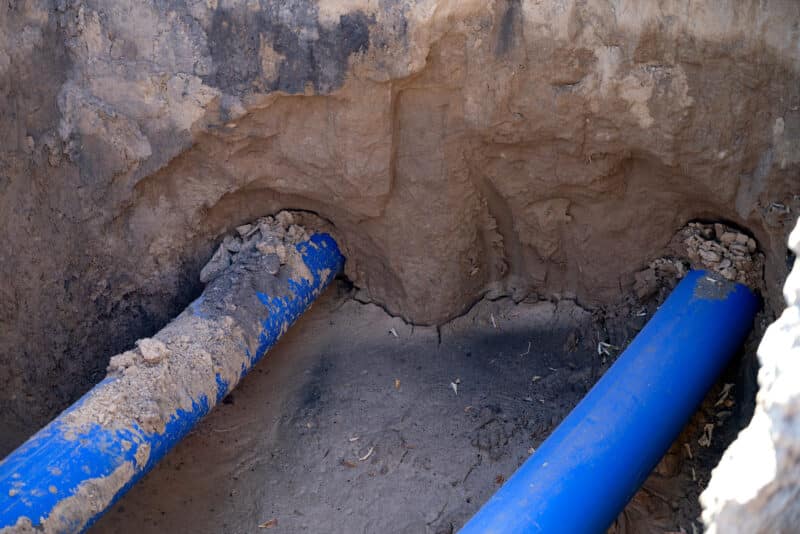 Newly installed blue PVC sewer pipe joined in an open excavation trench during a sewer line repair.