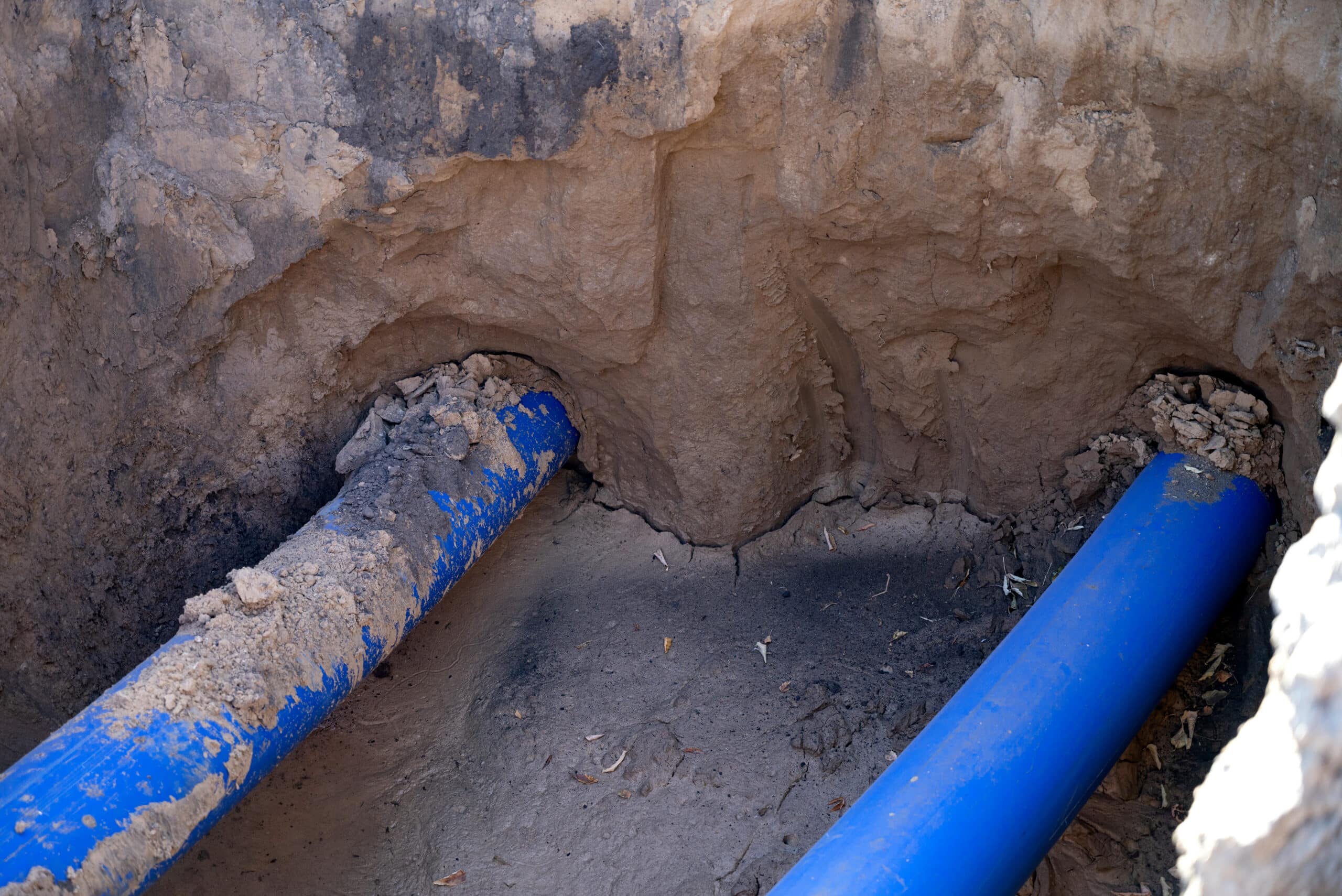 Newly installed blue PVC sewer pipe joined in an open excavation trench during a sewer line repair.