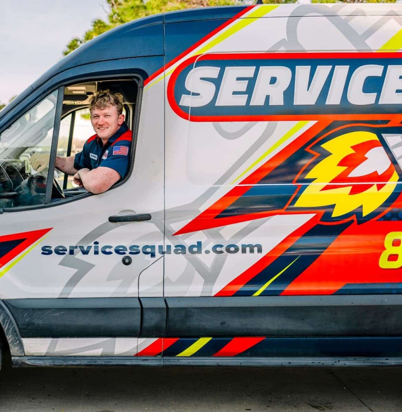 A smiling plumber sits in the driver&rsquo;s seat of a Service Squad van, ready for a service call.