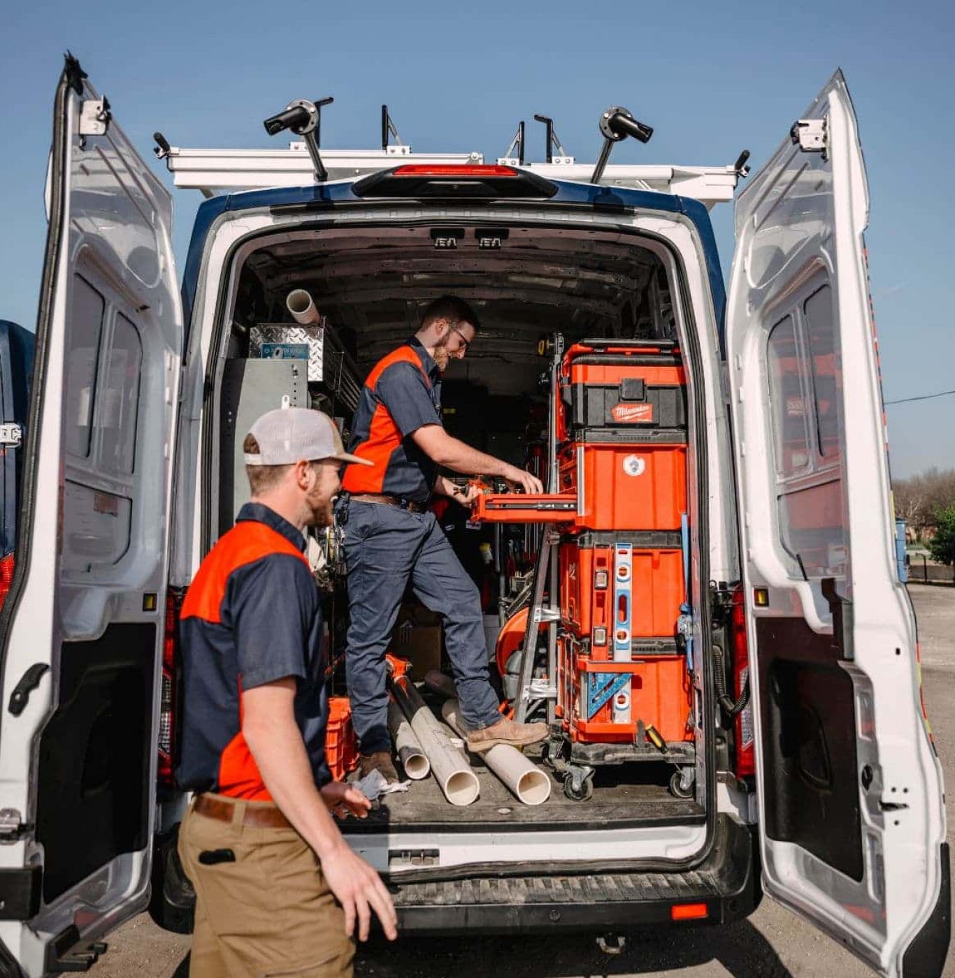 Two plumbers organizing tools inside a work van